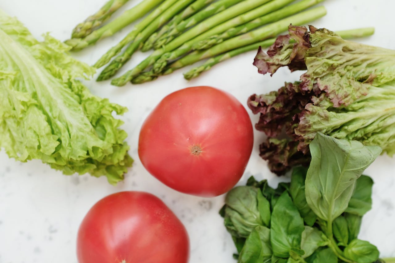 Top view of fresh asparagus, lettuce, basil, and tomatoes, highlighting healthy and nutritious ingredients.