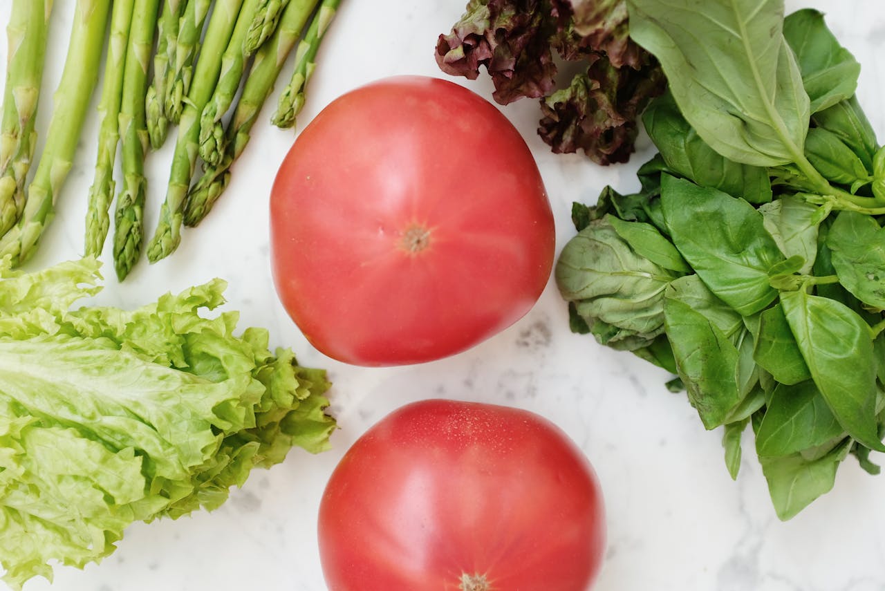 A vibrant collection of fresh vegetables including tomatoes, asparagus, and leafy greens on a marble surface.